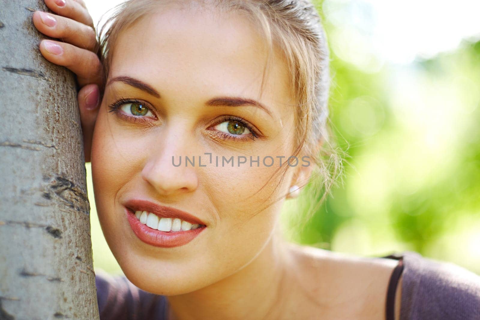 Portrait of charming girl looking at camera by tree trunk