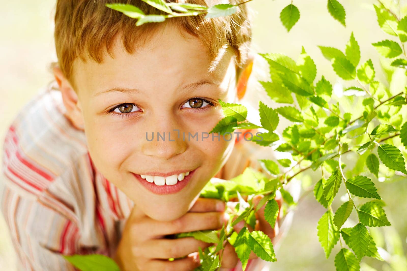 Portrait of handsome schoolboy smiling at camera out of green branch