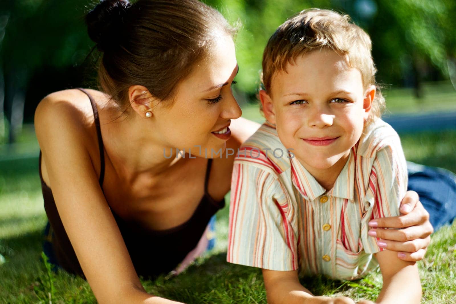 Portrait of happy boy smiling at camera while being embraced by his mother