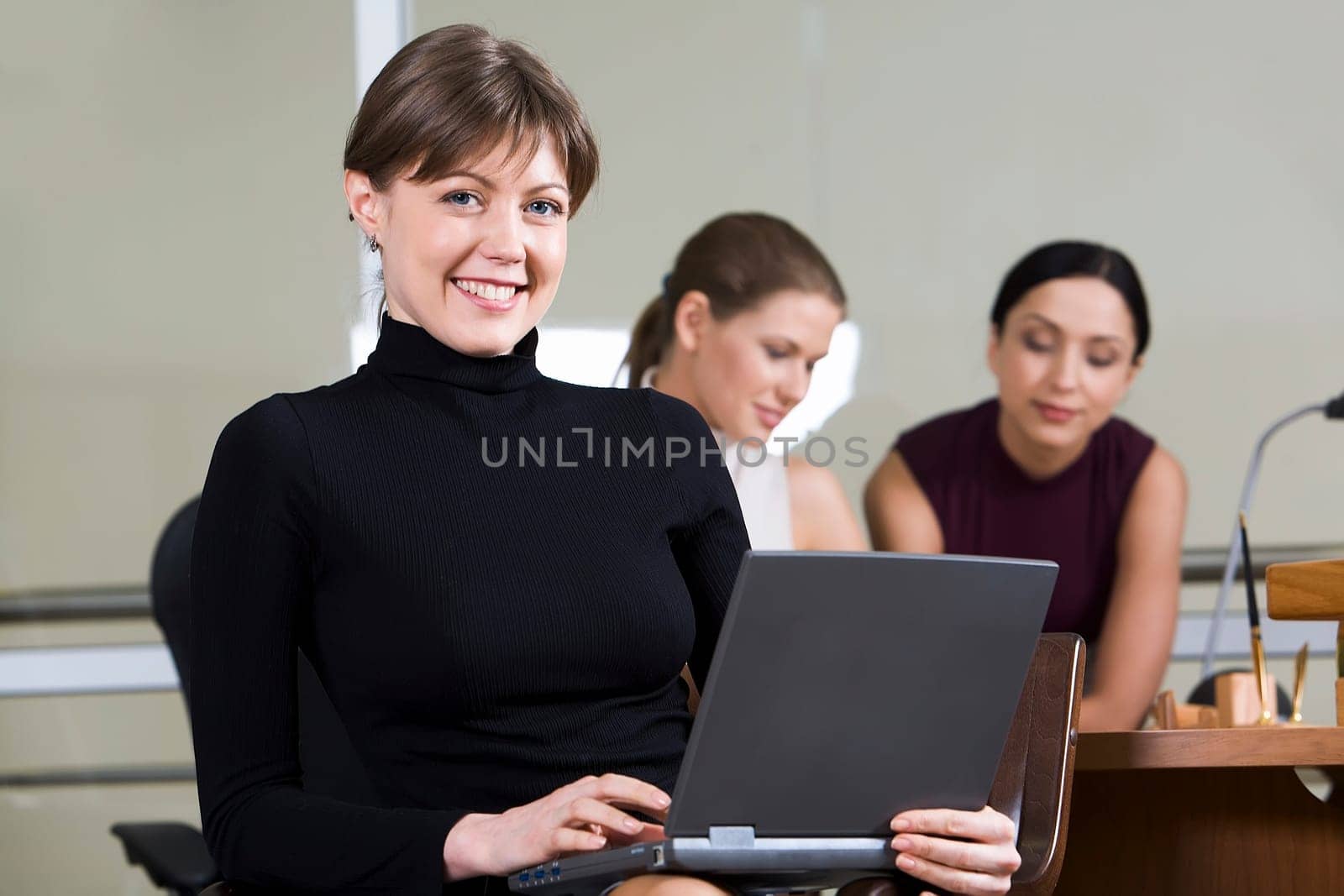 Portrait of smiling woman with the laptop on her knees sitting in the cafe and two girls on the background