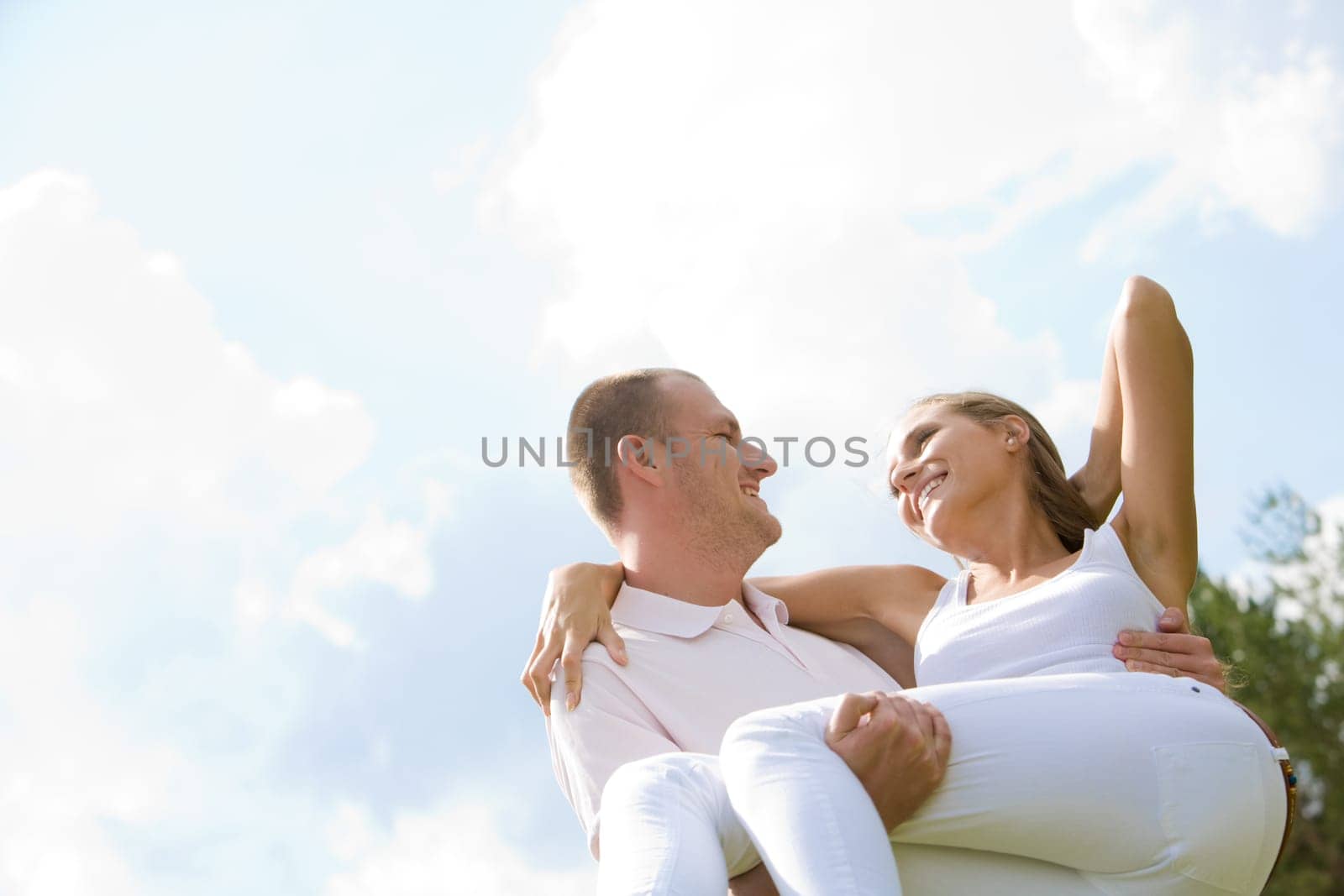 Happy male holding his girlfriend on hands with blue sky above