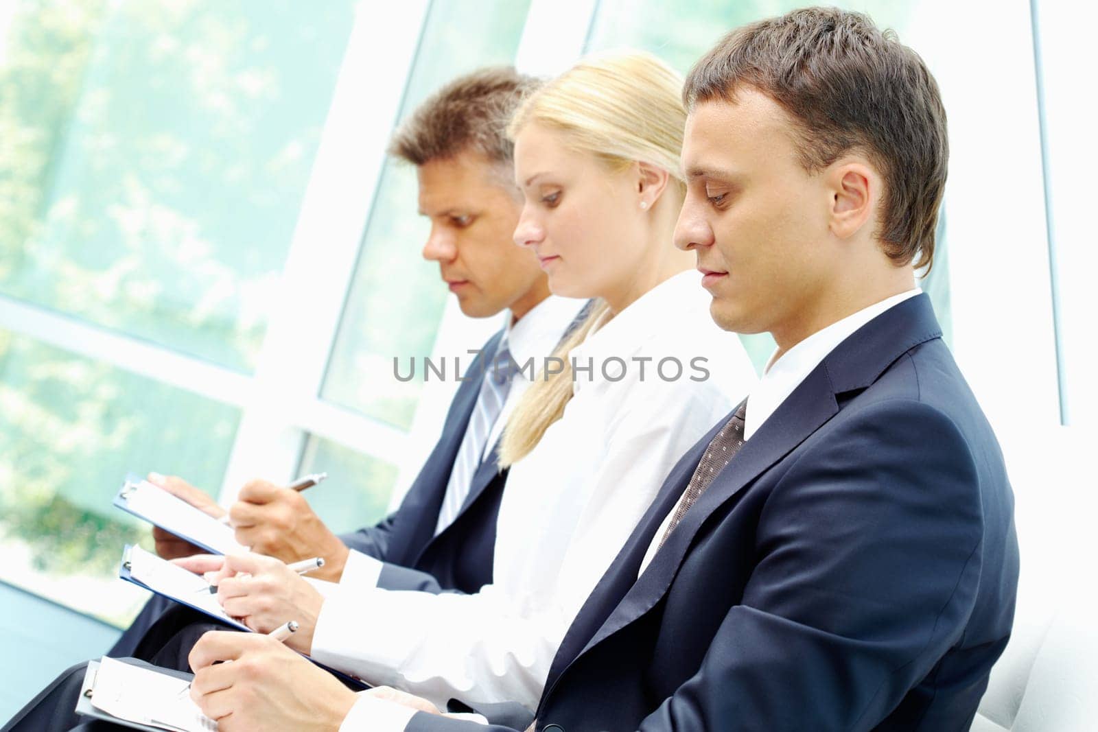 Row of three employees writing at conference with serious man on foreground