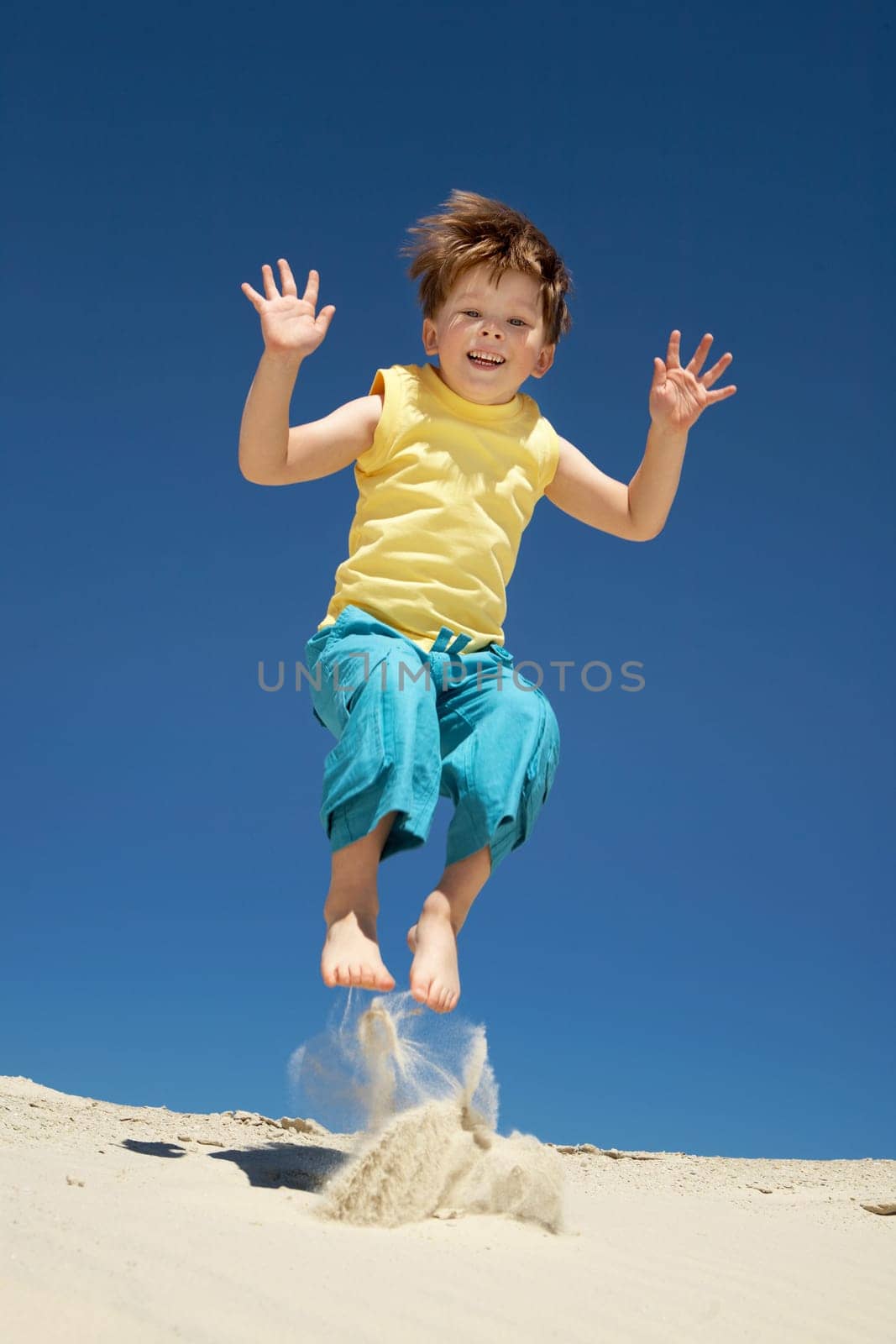 Happy boy jumping on sand and looking at camera with smile during summer vacations