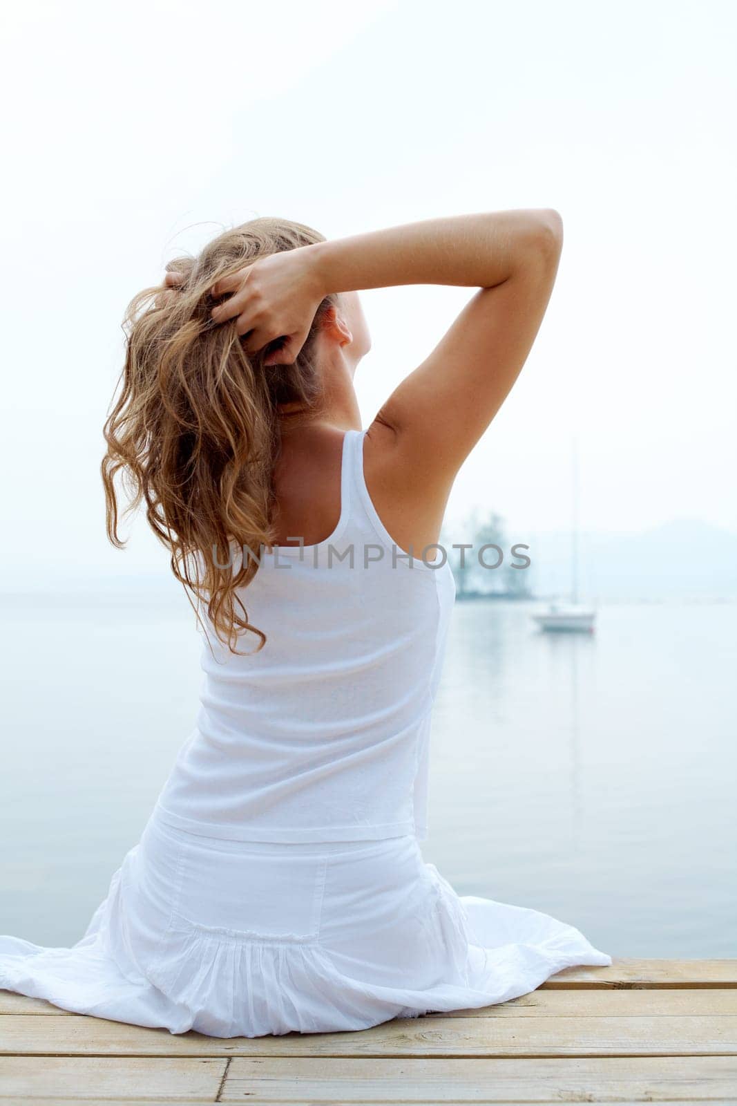 Rear view of pretty young lady in white cotton clothes having rest by the seaside