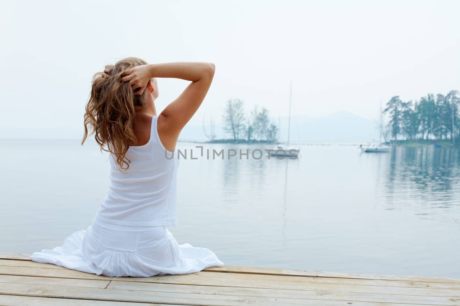 Rear view of pretty young lady in white cotton clothes having rest by the seaside