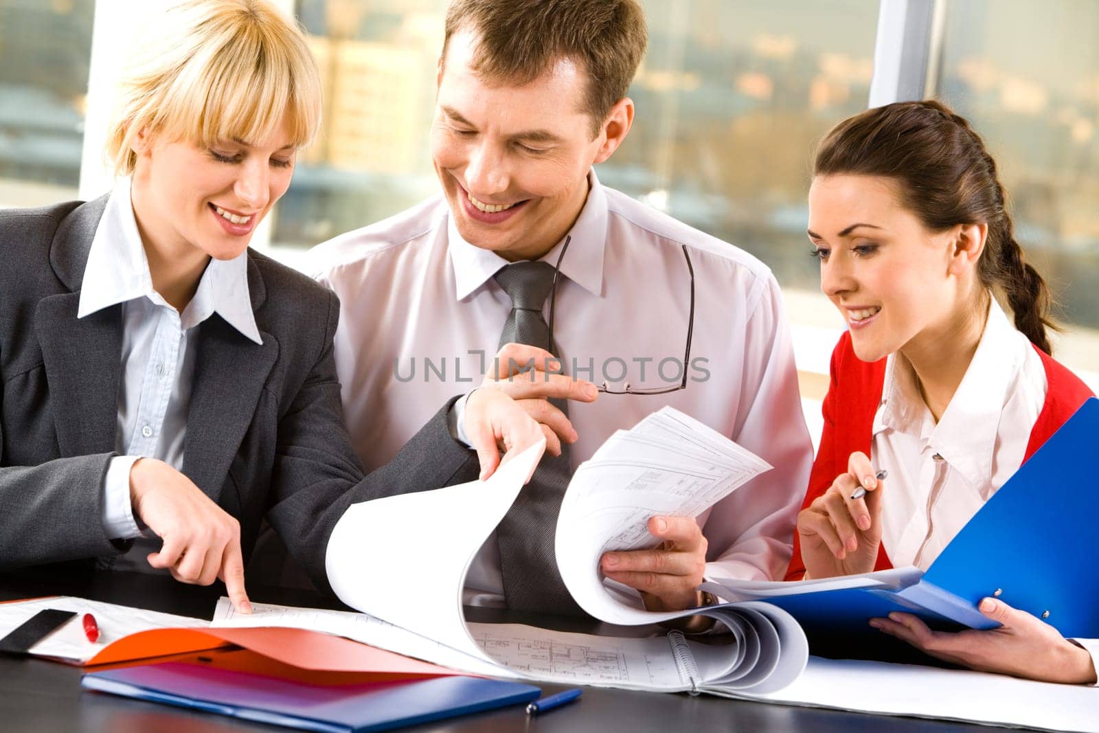 Two business ladies and a businessman looking through their business documents and discussing them smiling