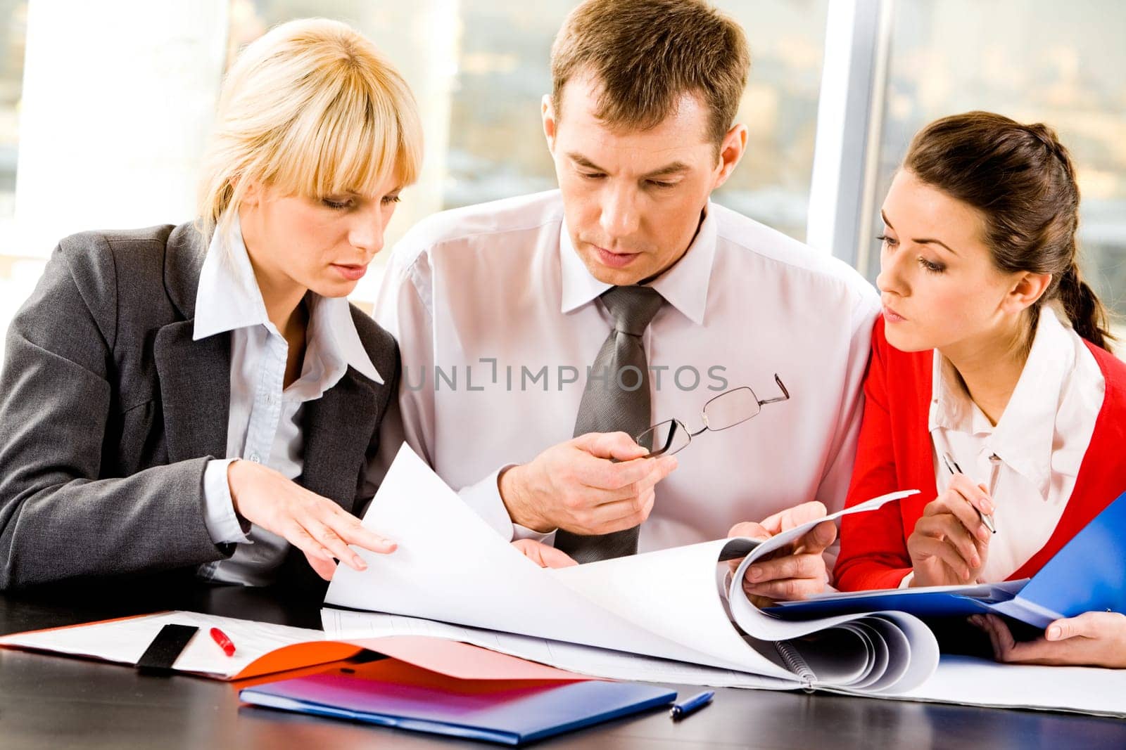 Team of three business people sitting at the table with several documents and discussing important questions