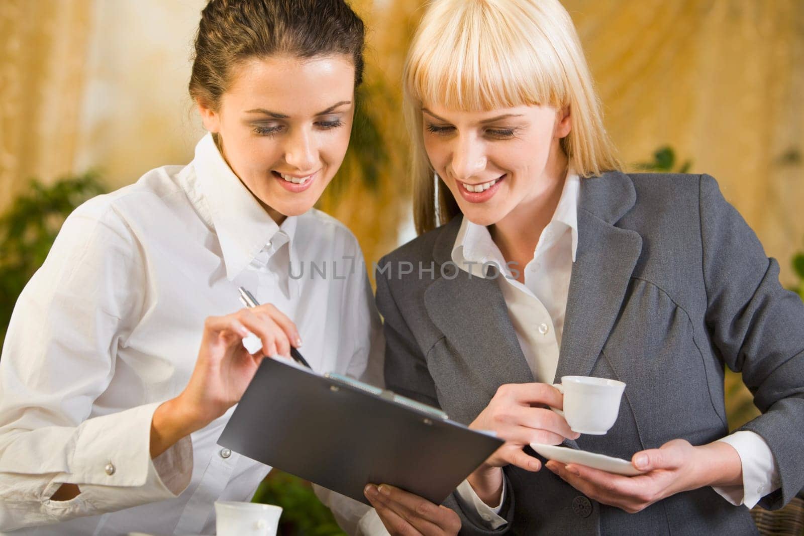 Two smiling attractive young business women are chatting