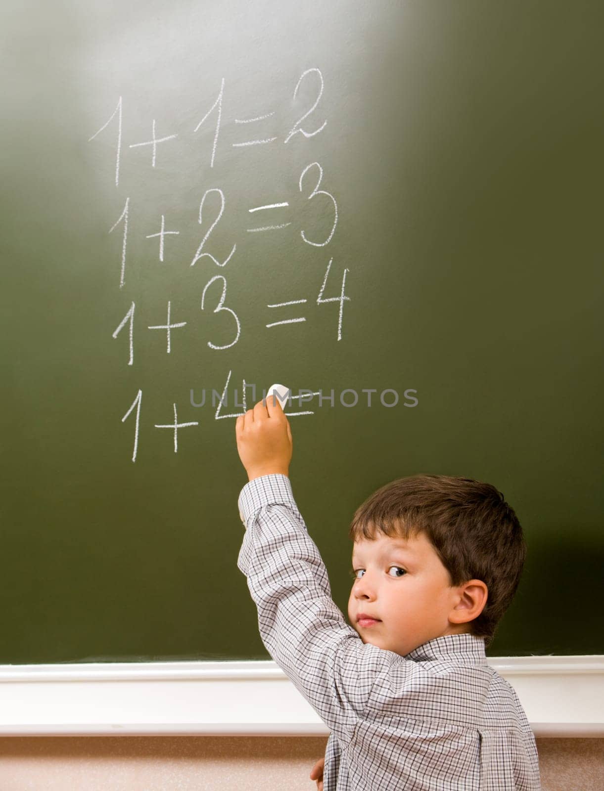 Portrait of pensive schoolchild standing at blackboard and doing sums