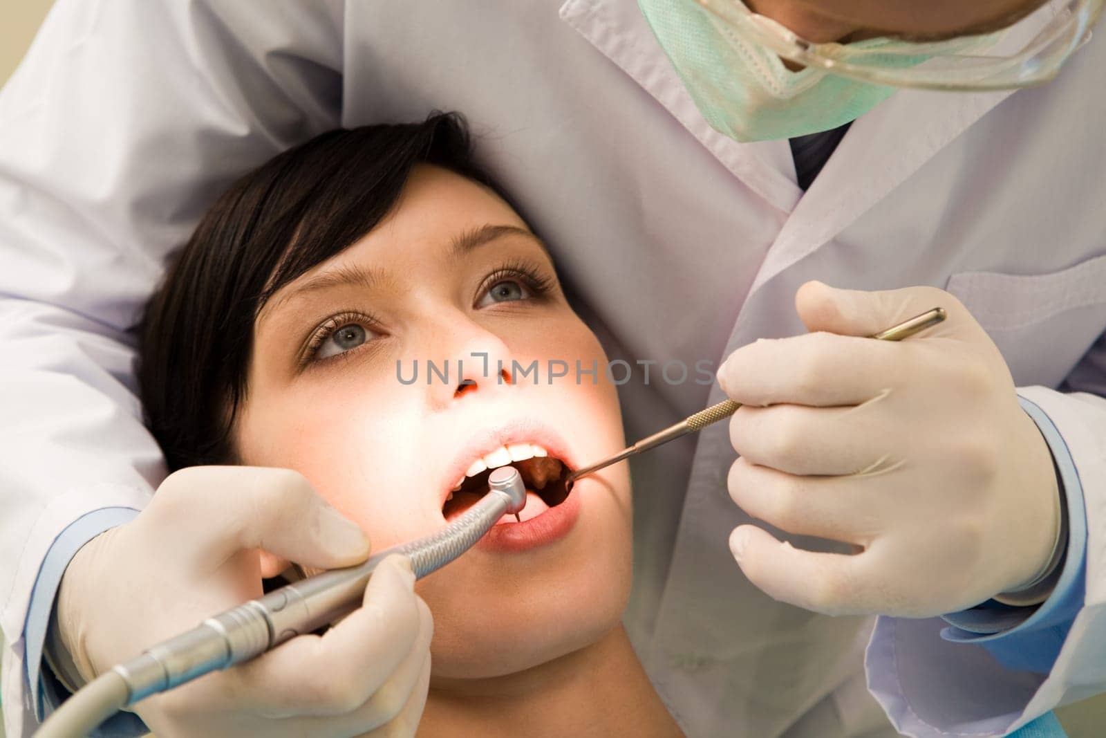 Image of young woman keeping her mouth open while dentist examining it