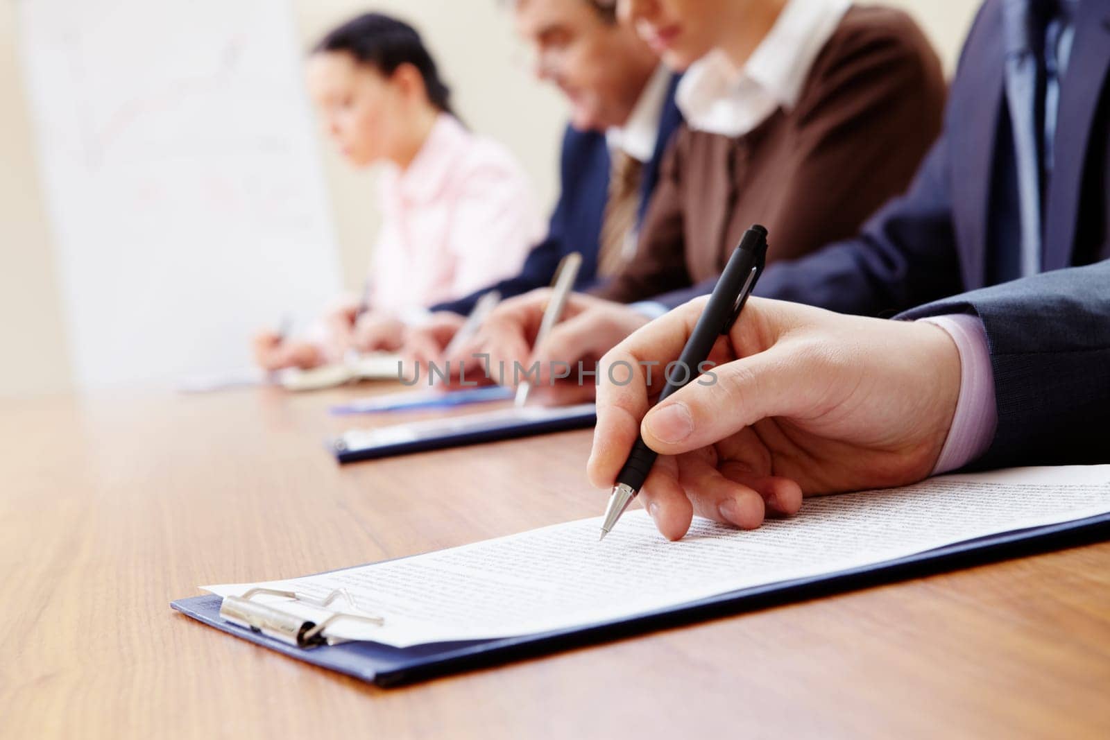 Row of business people making notes with focus on hand holding pen