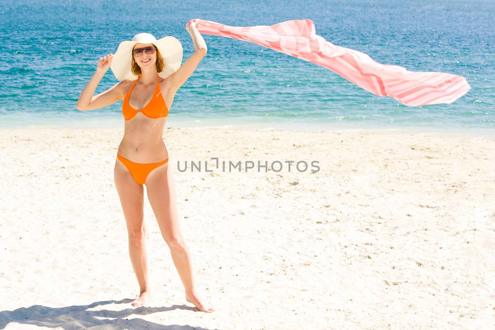 Photo of cheerful woman standing on the beach with pareo in hand