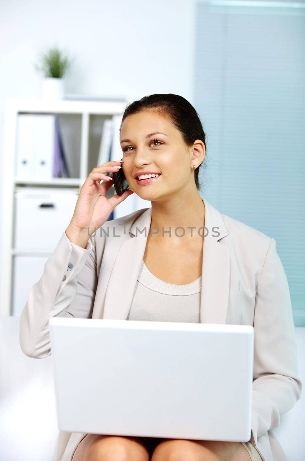 Image of young employer speaking on the phone with laptop on her knees