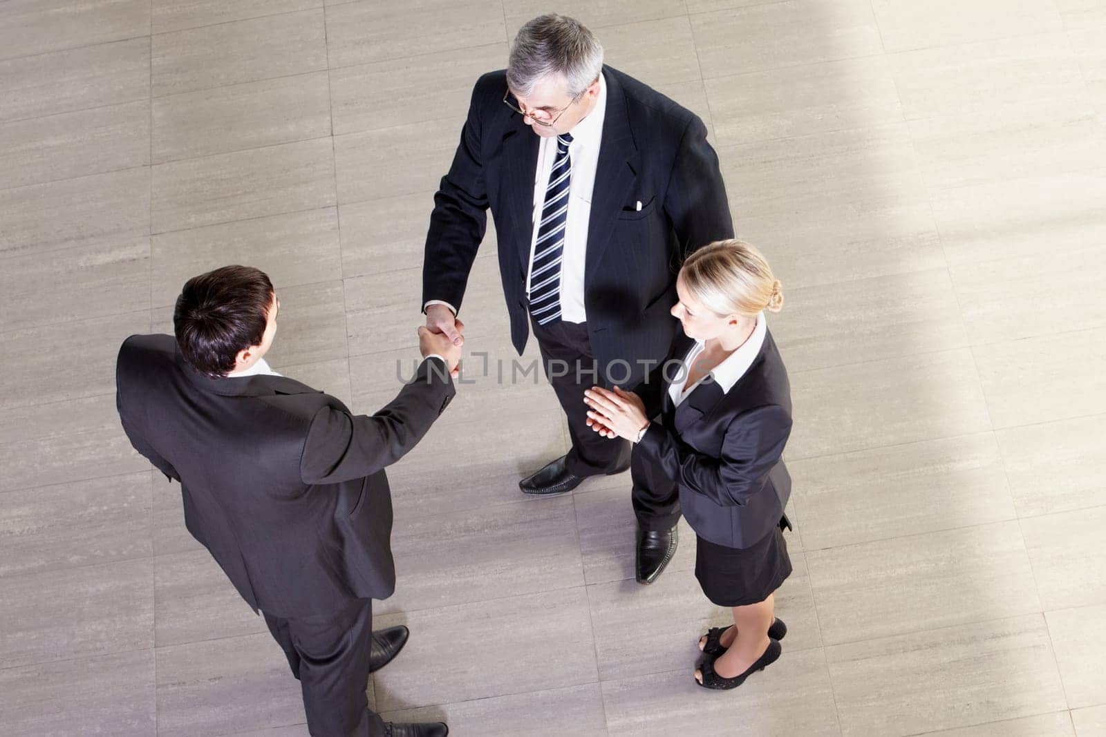 Senior manager shaking hands with his partner, their colleague clapping