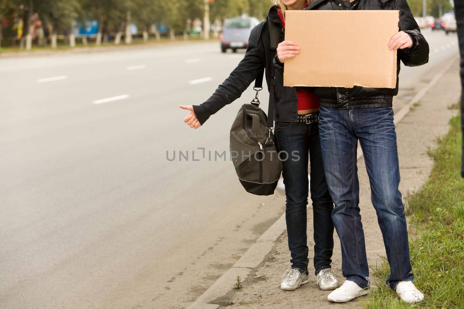 Photo of traveling couple with message board hitchhiking on city road