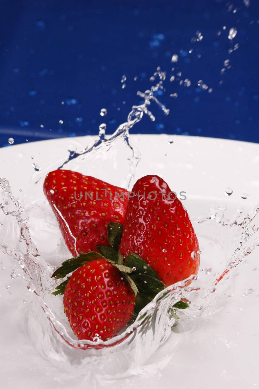 3 strawberries splashing in water