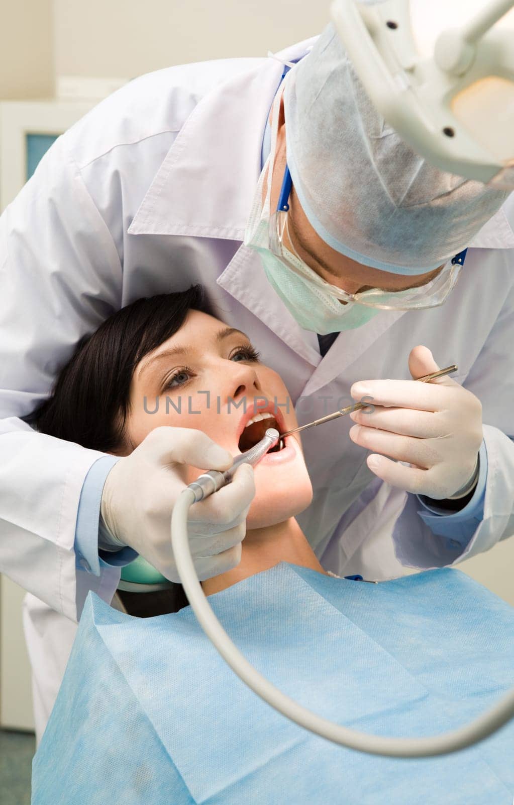 Vertical image of female patient with dentist over her checking up teeth and drilling them