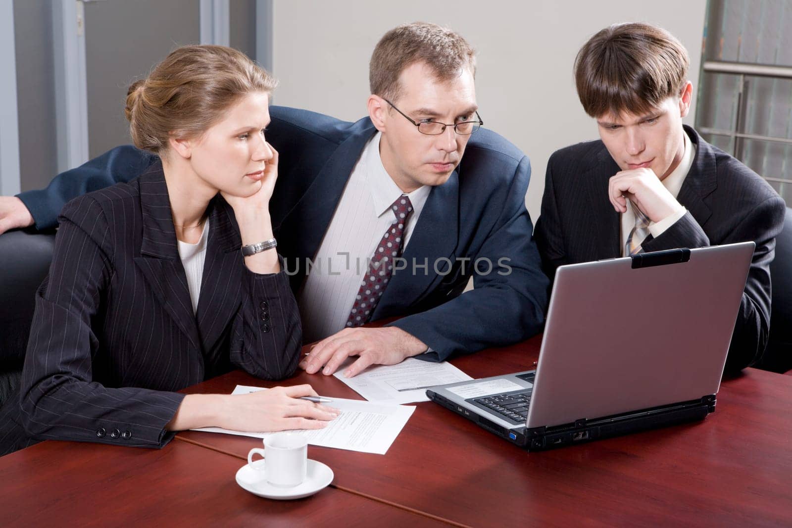 Business team of three professionals looking at monitor of laptop in the office