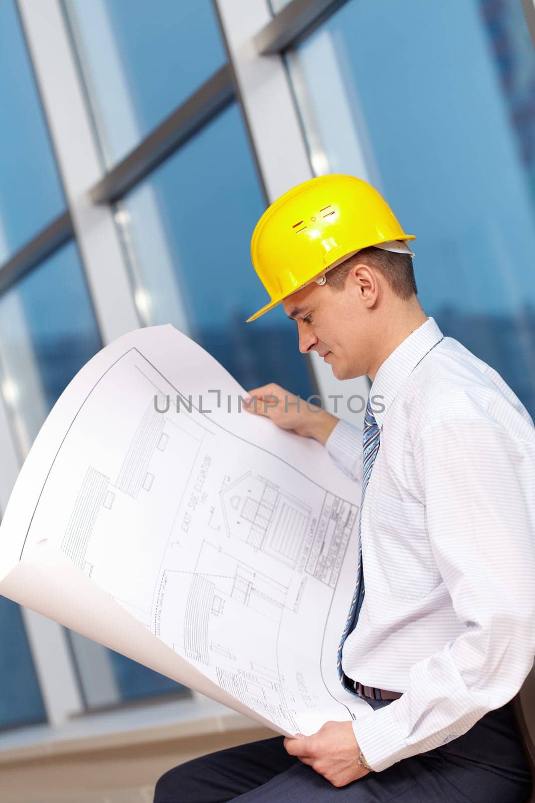 A young architect in helmet looking at blueprint