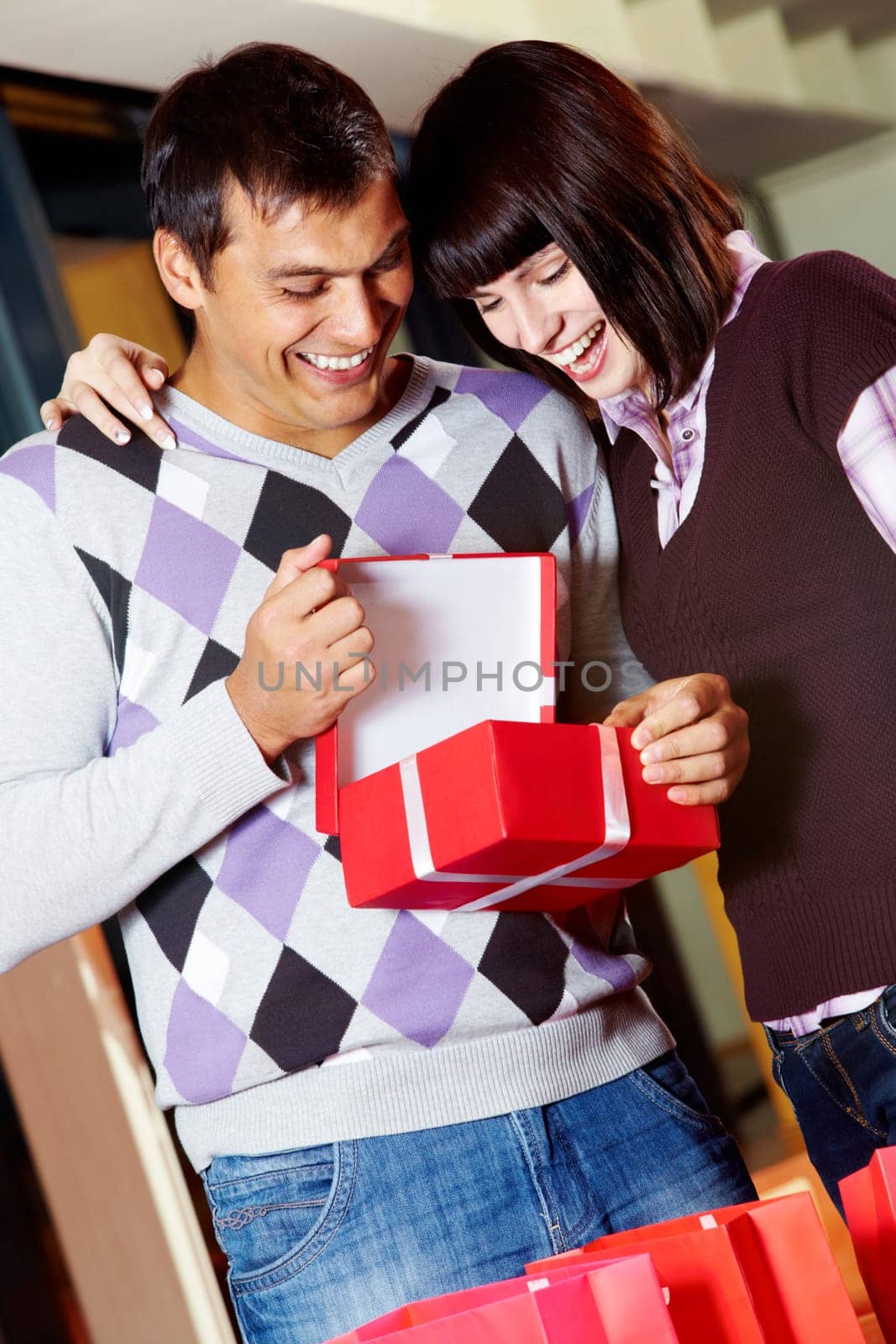 Happy girl and handsome man looking into open red giftbox with smiles