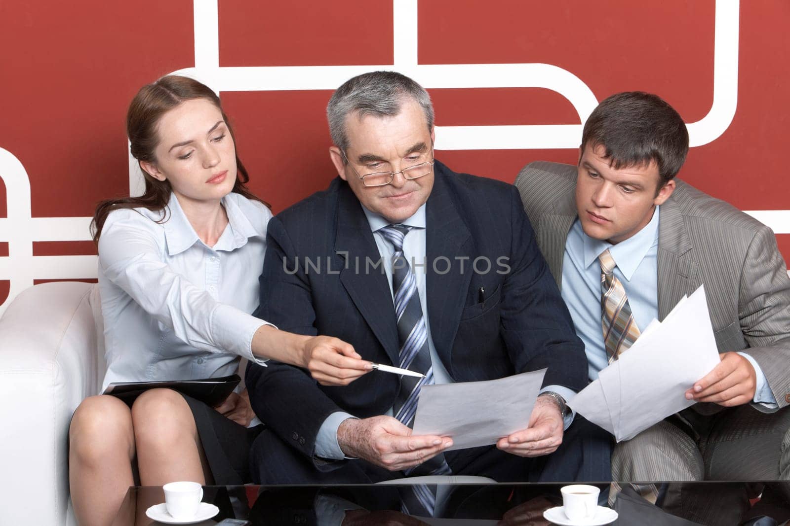Serious men looking with interest into business plan in chiefs hands at which pretty woman pointing while sitting on sofa