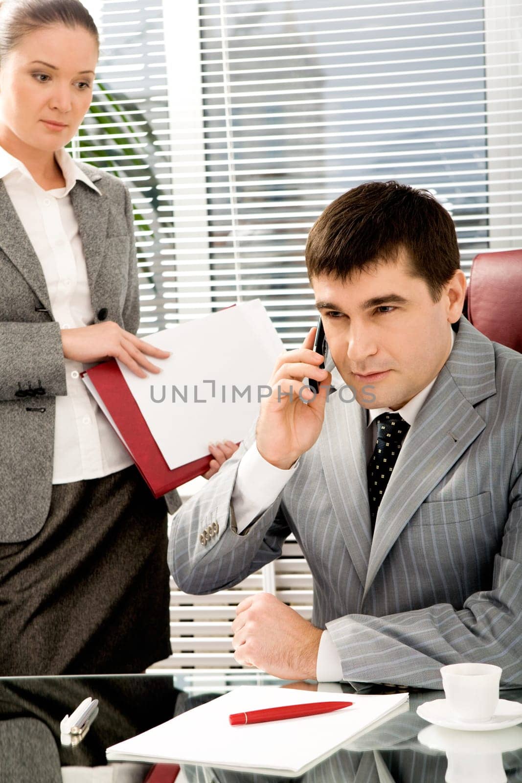 Portrait of confident boss talking on the phone with executive secretary standing near by