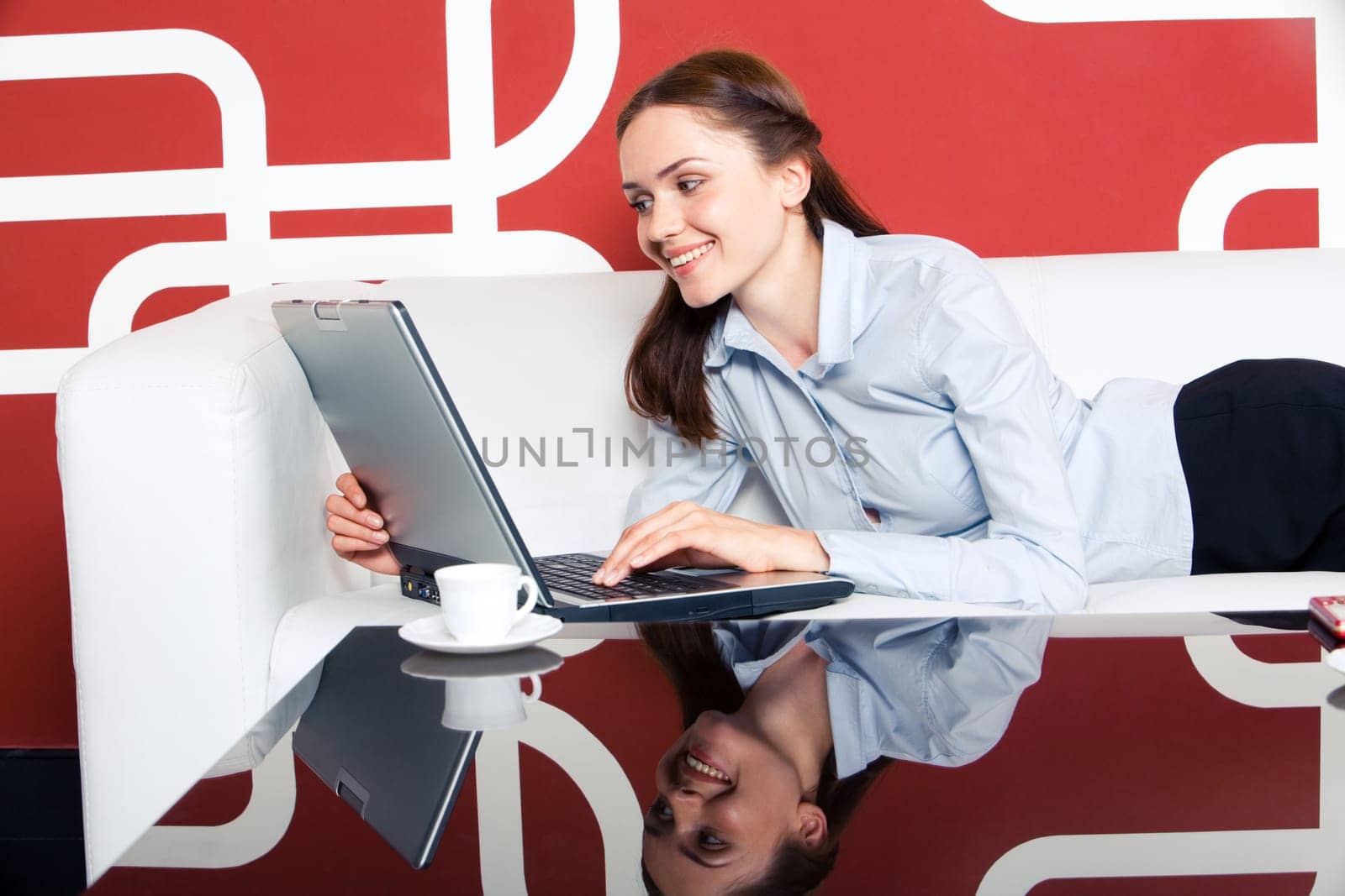 Photo of pretty business lady lying on sofa with laptop in front and looking at its monitor with smile