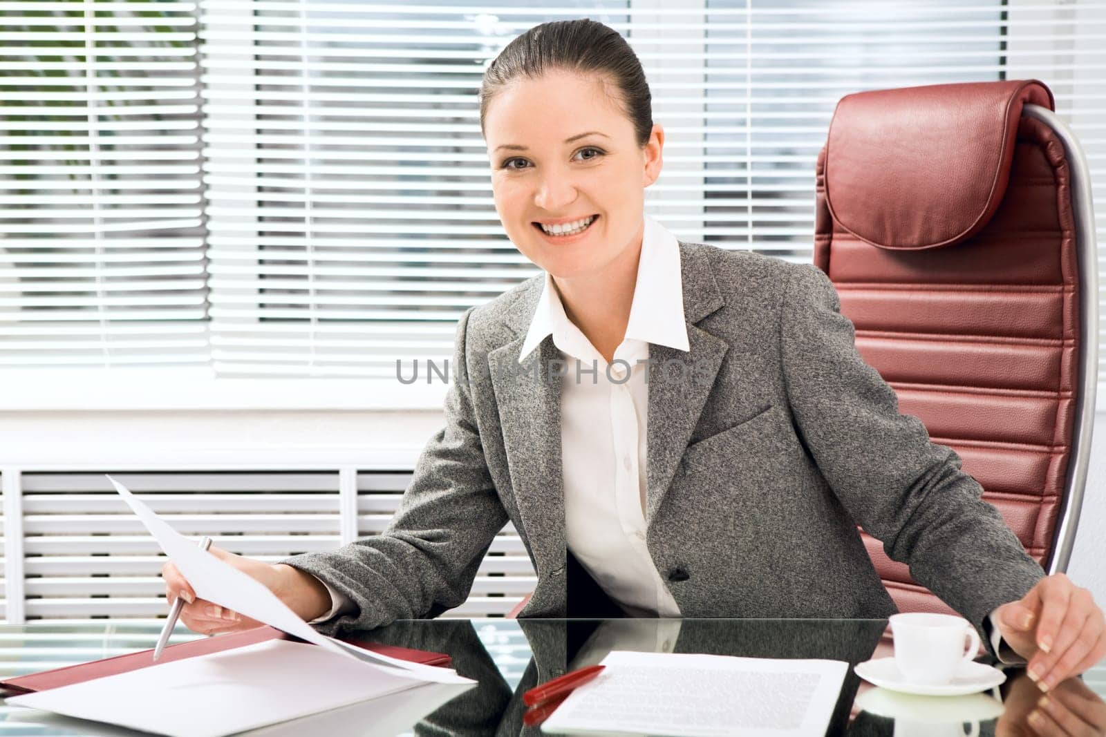 Portrait of successful businesswoman holding document while looking at camera with smile in office