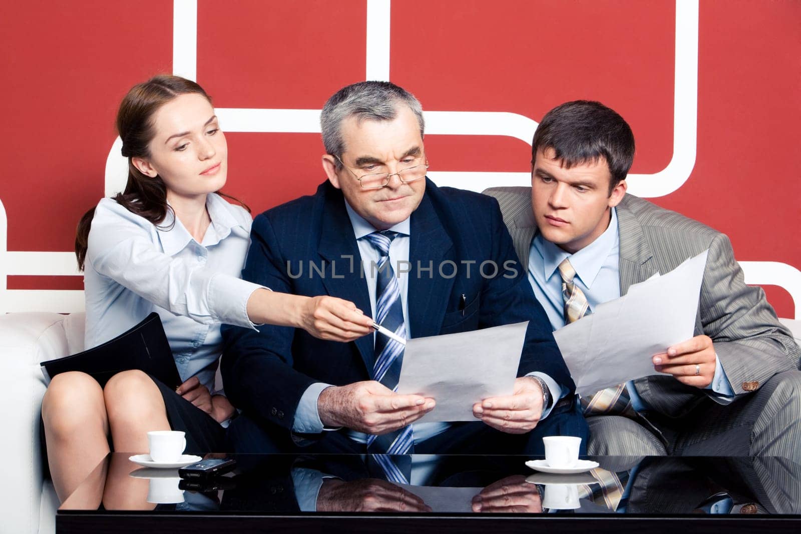 Serious men looking with interest into business plan in chiefs hands at which pretty woman pointing while sitting on sofa