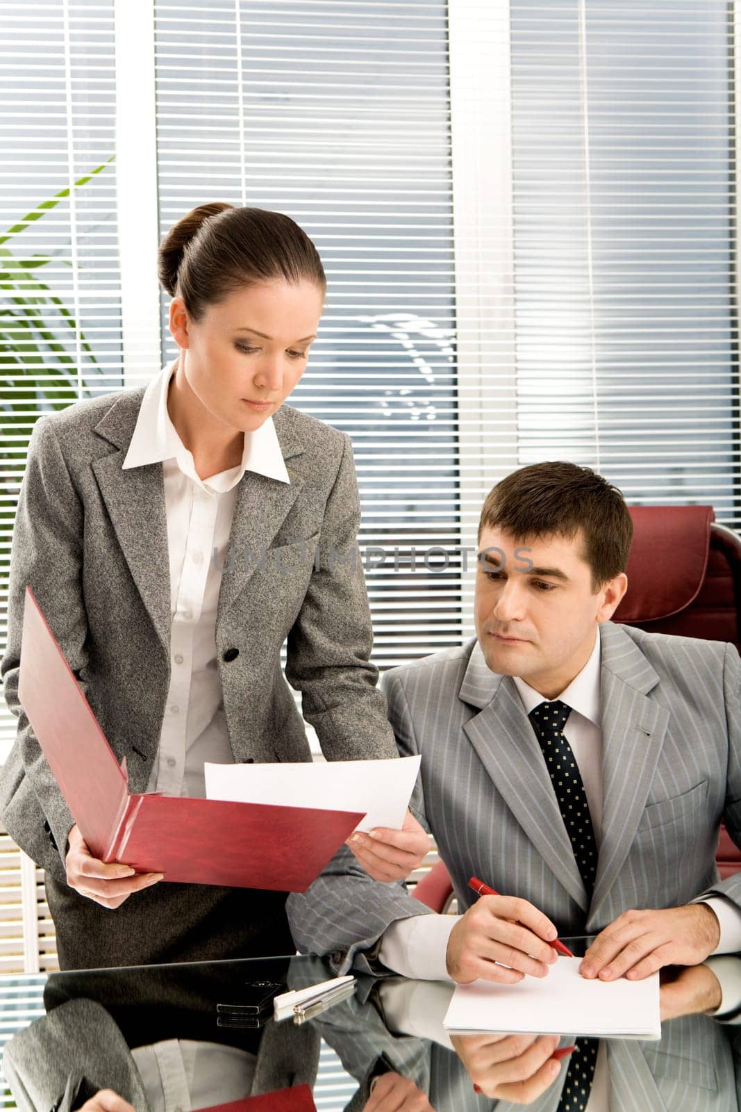 Pretty secretary showing papers to her boss in office