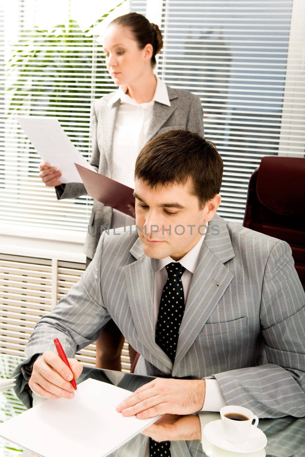 Portrait of serious boss signing contract with executive secretary on background