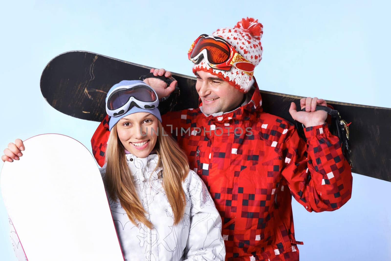Portrait of happy couple with snowboards on blue background