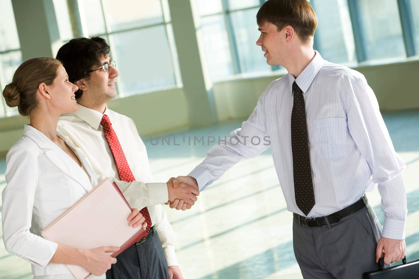 Portrait of businessmen shaking hands at meeting with businesswoman near by