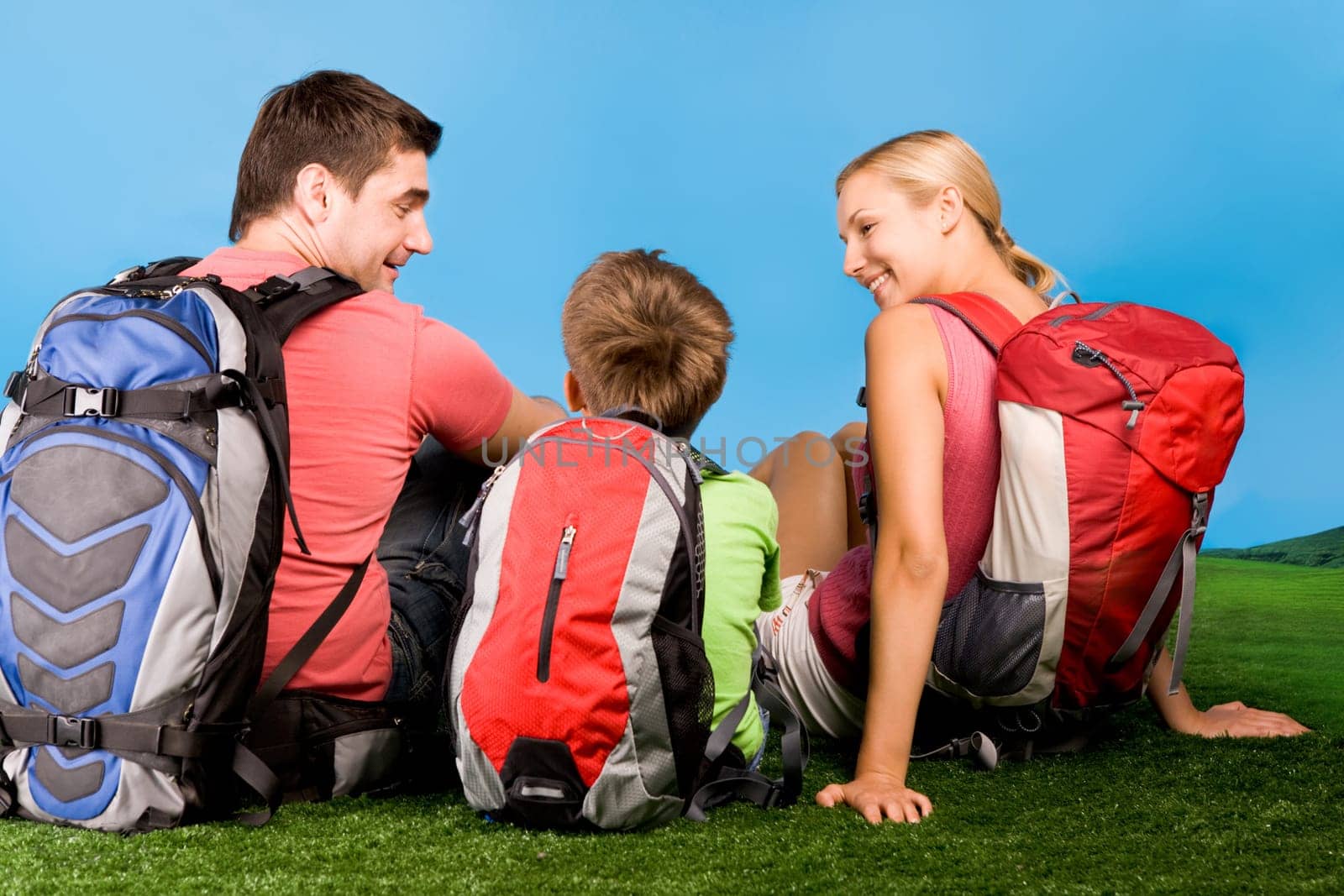 Rear view of family chatting on grassland during rest over blue background