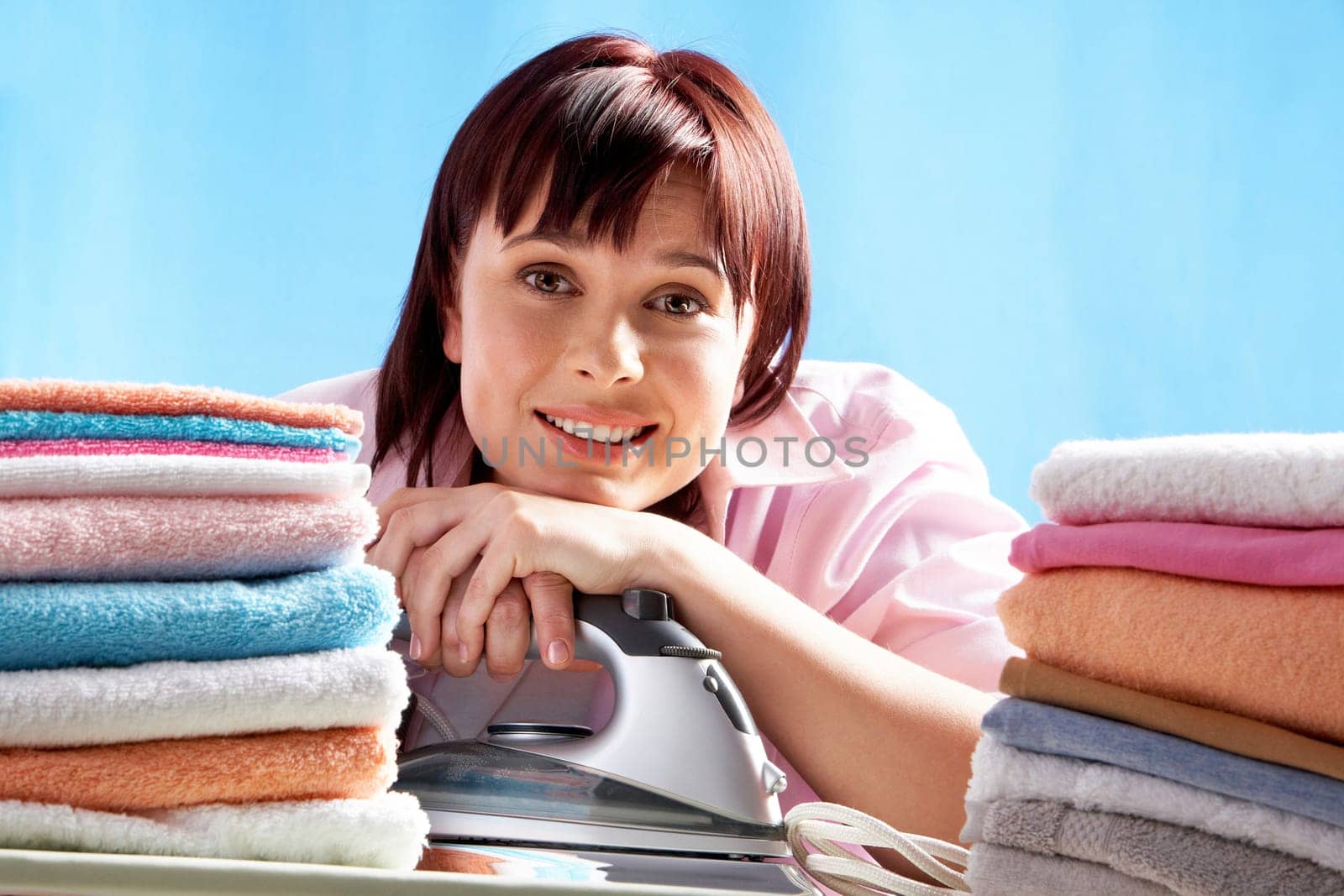 A smiling woman with an iron and heaps of ironed towels