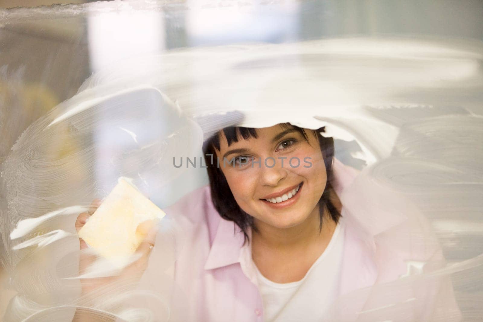 Portrait of young female washing window and smiling