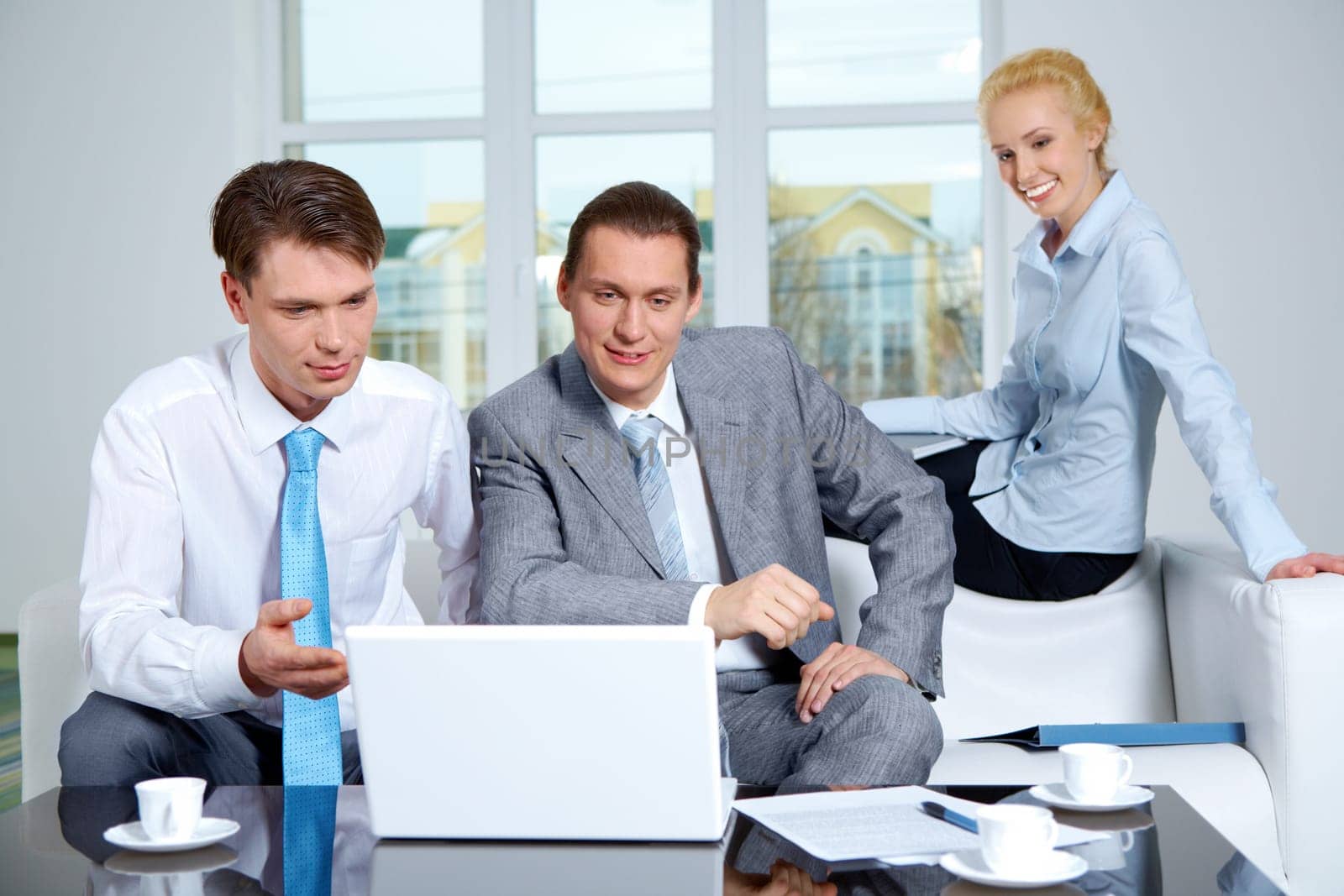 Portrait of successful co-workers sharing their ideas in office while looking at laptop monitor