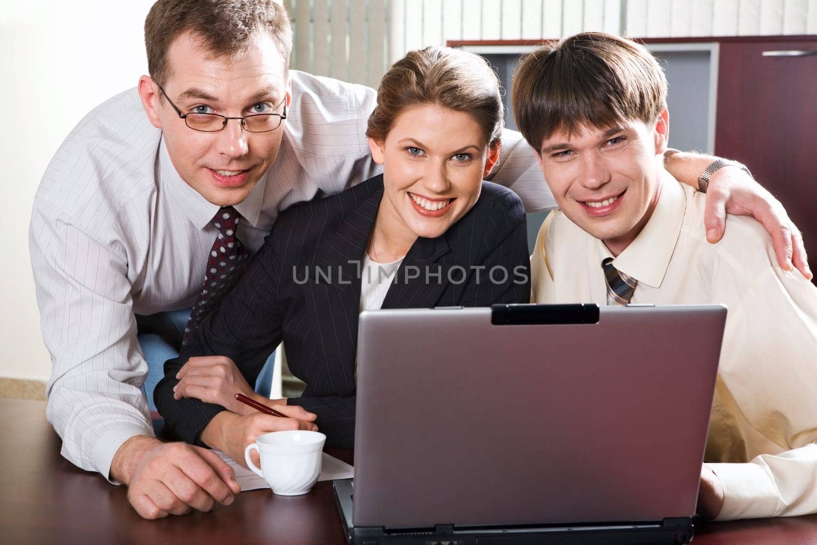 Three smiling businessmen at the table looking at the camera