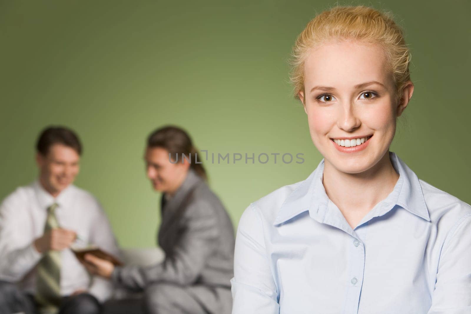 Portrait of blond girl looking at camera with two interacting businessmen at background