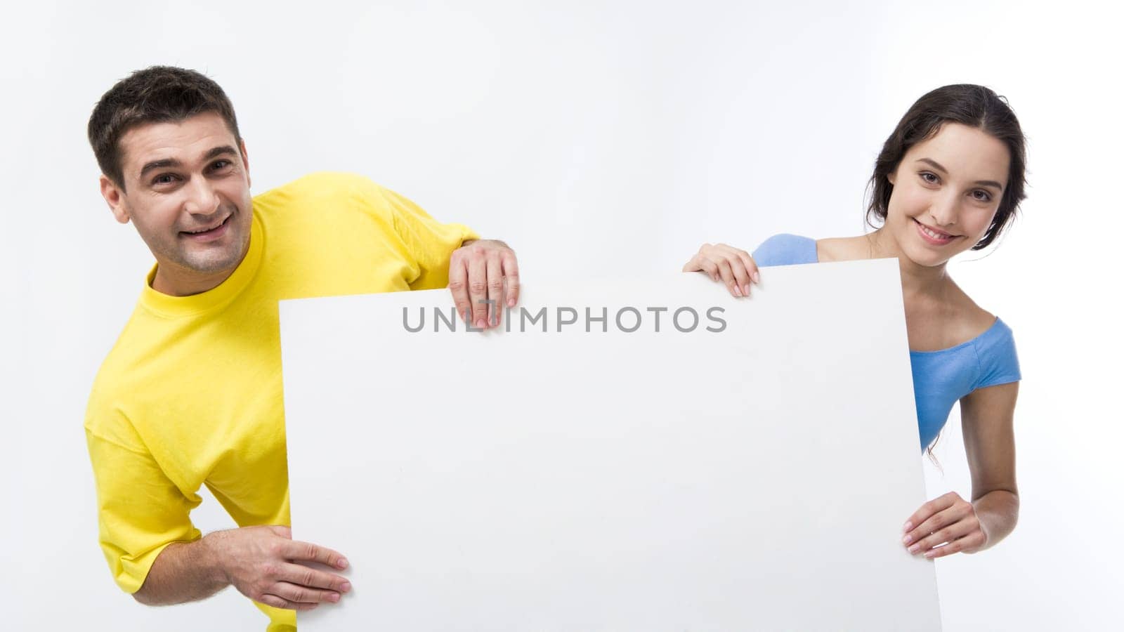 Smiling couple holding blank poster and looking at camera on white background