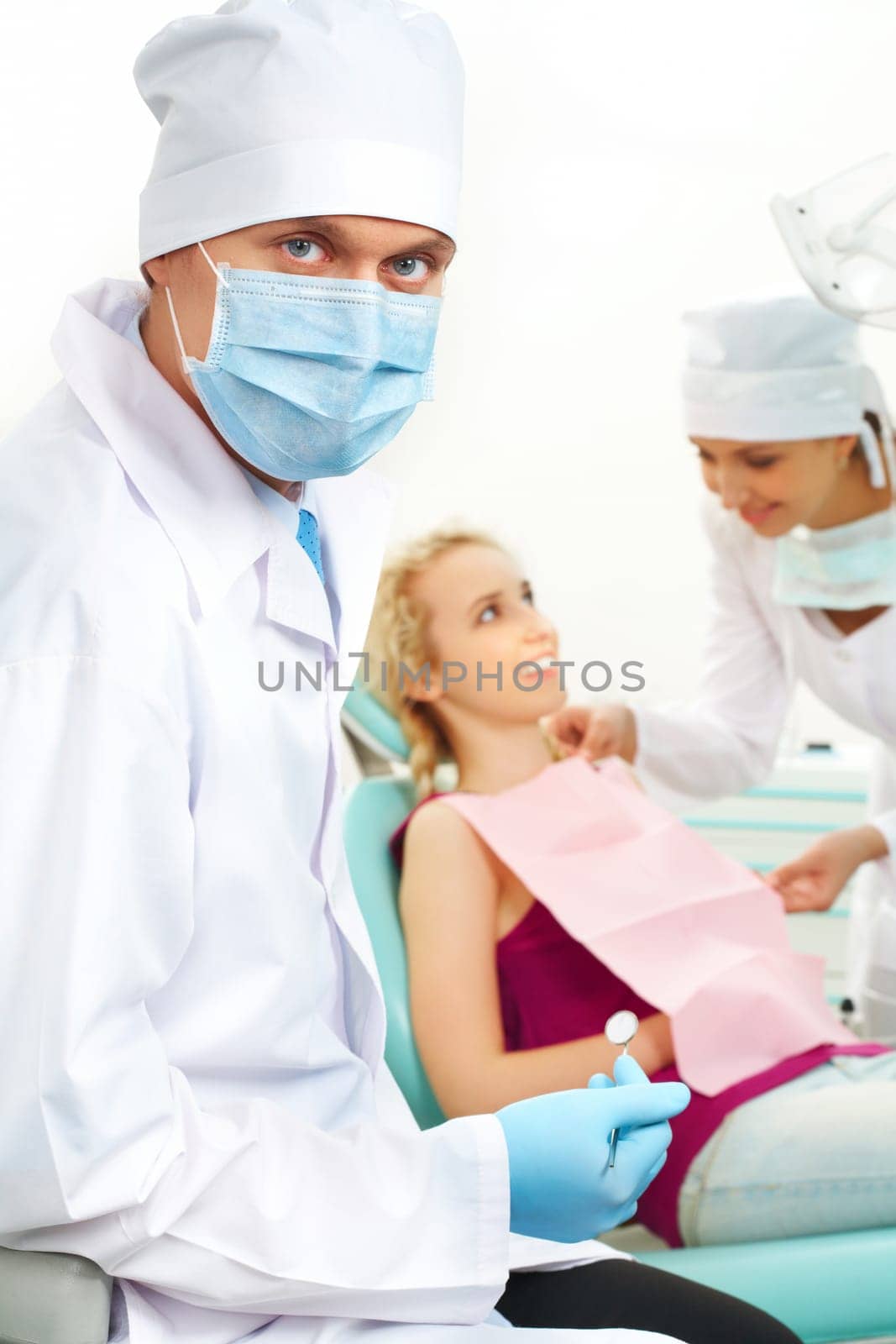 Portrait of confident doctor in sterile mask on background of his assistant helping patient