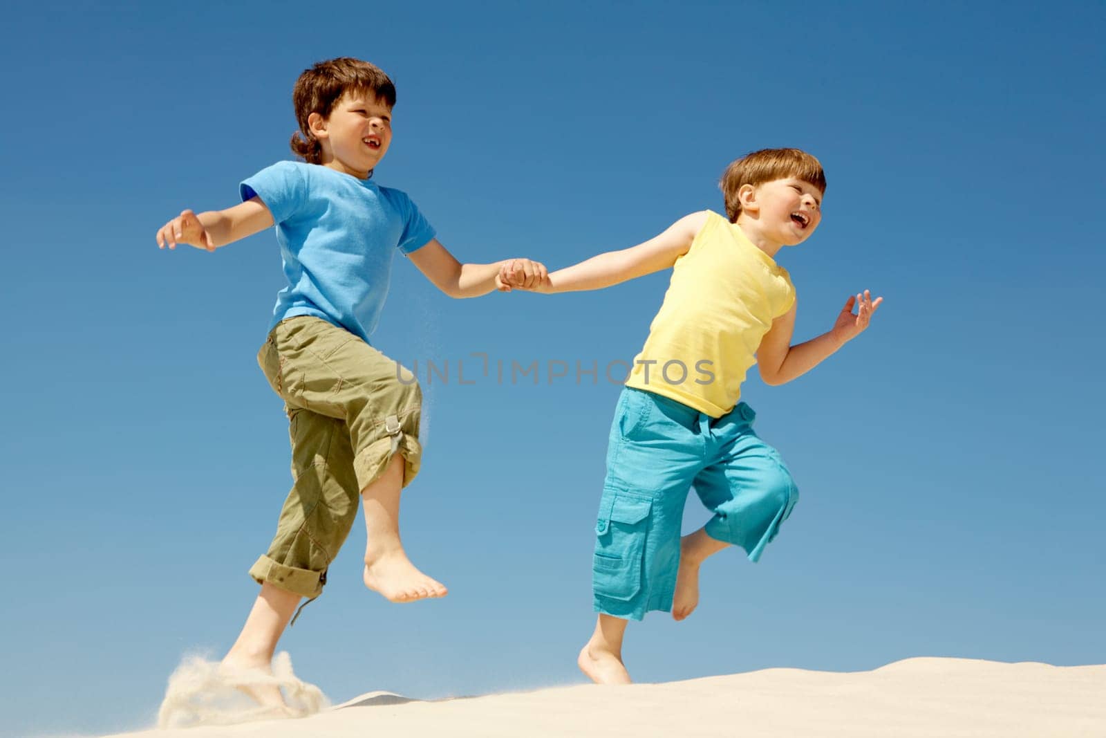 Photo of happy boys running down sandy beach and laughing