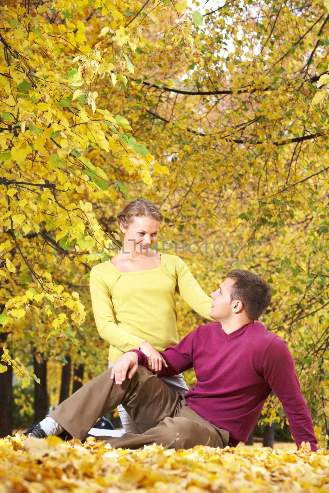 Young couple sitting together on leaves in autumn park