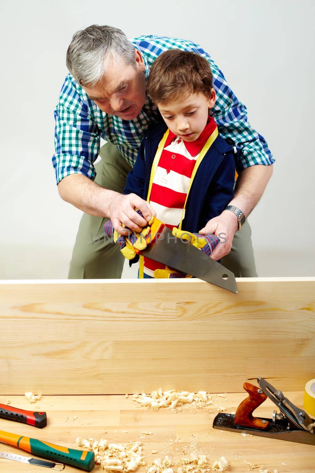 A grandfather teaching a boy to work with saw