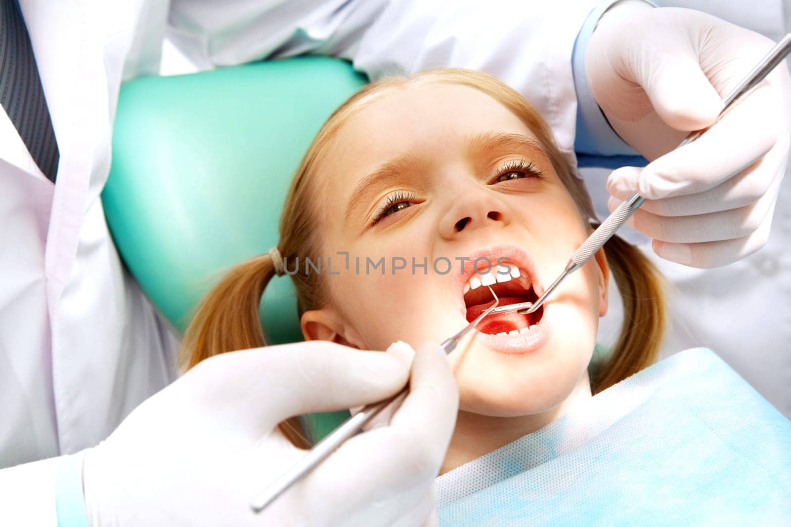 Photo of small girl with open mouth while it being examined by dentist