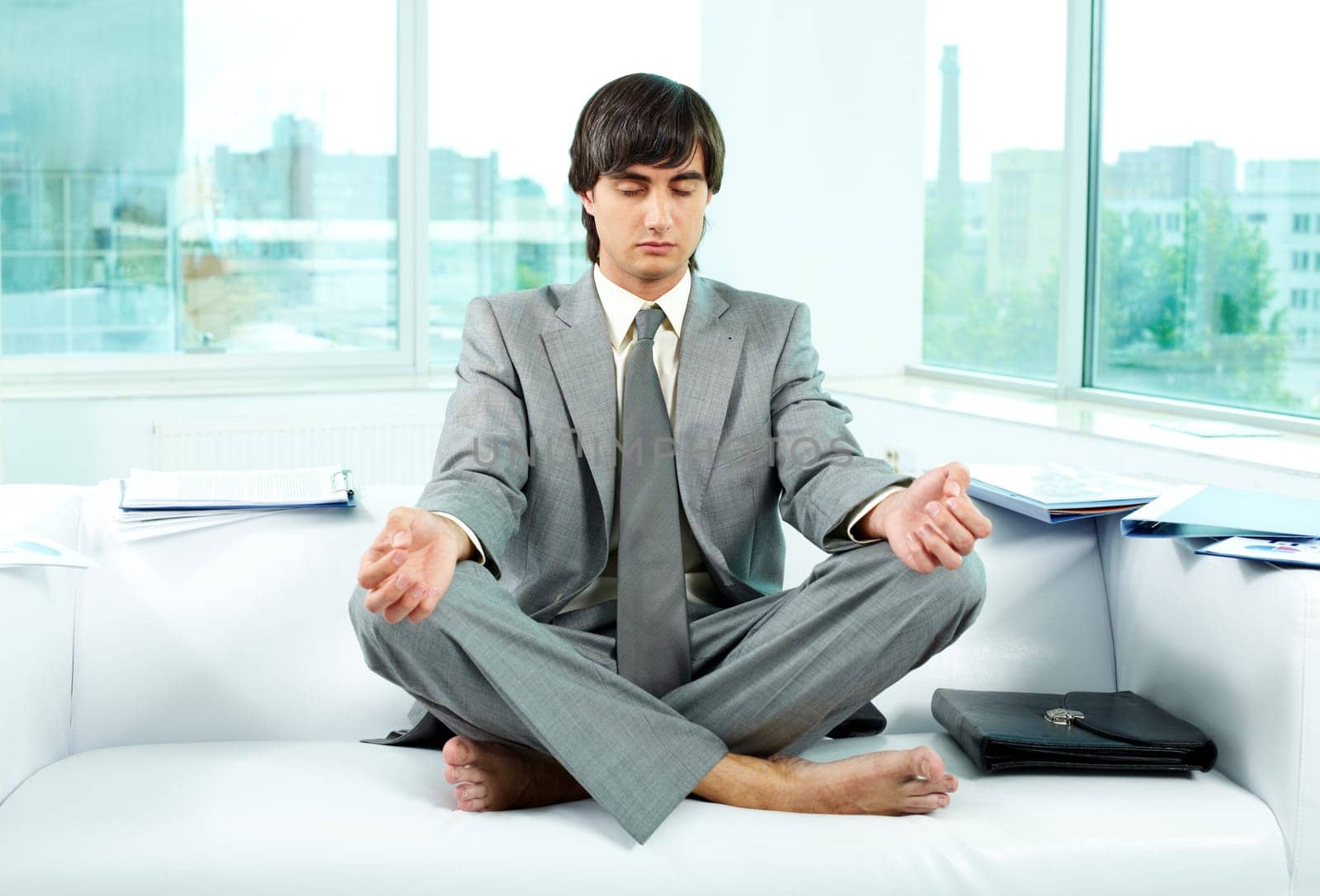 A young businessman meditating on sofa in office