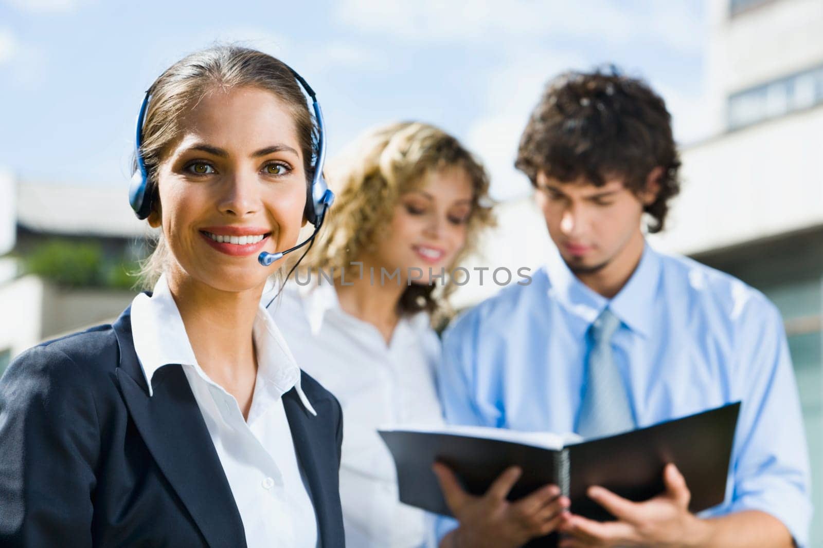 Portrait of smiling woman with headset on her head and two reading people on the background
