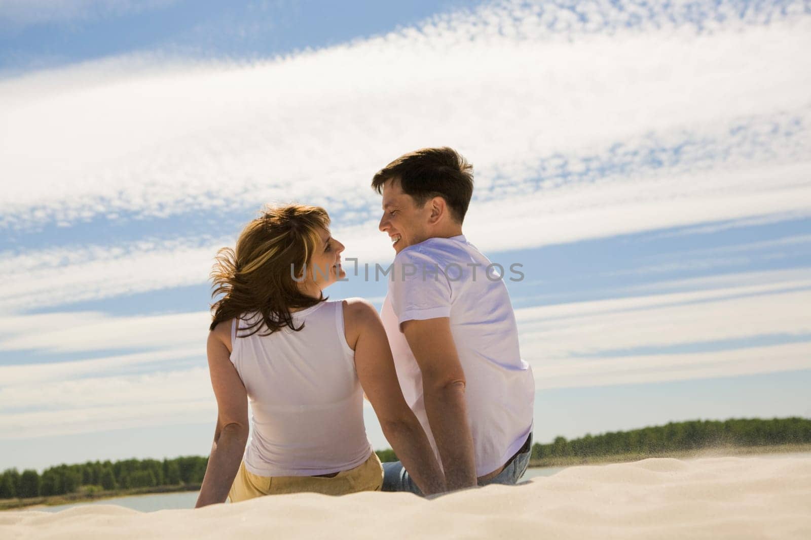 Rear view of relaxing couple sitting on sandy beach and smiling at each other