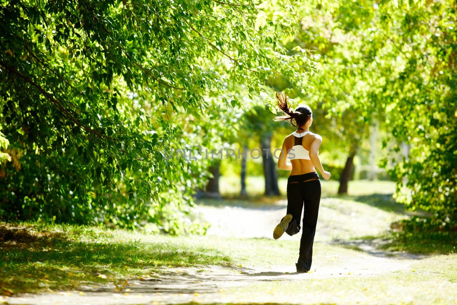 A young girl jogging in the park along trees