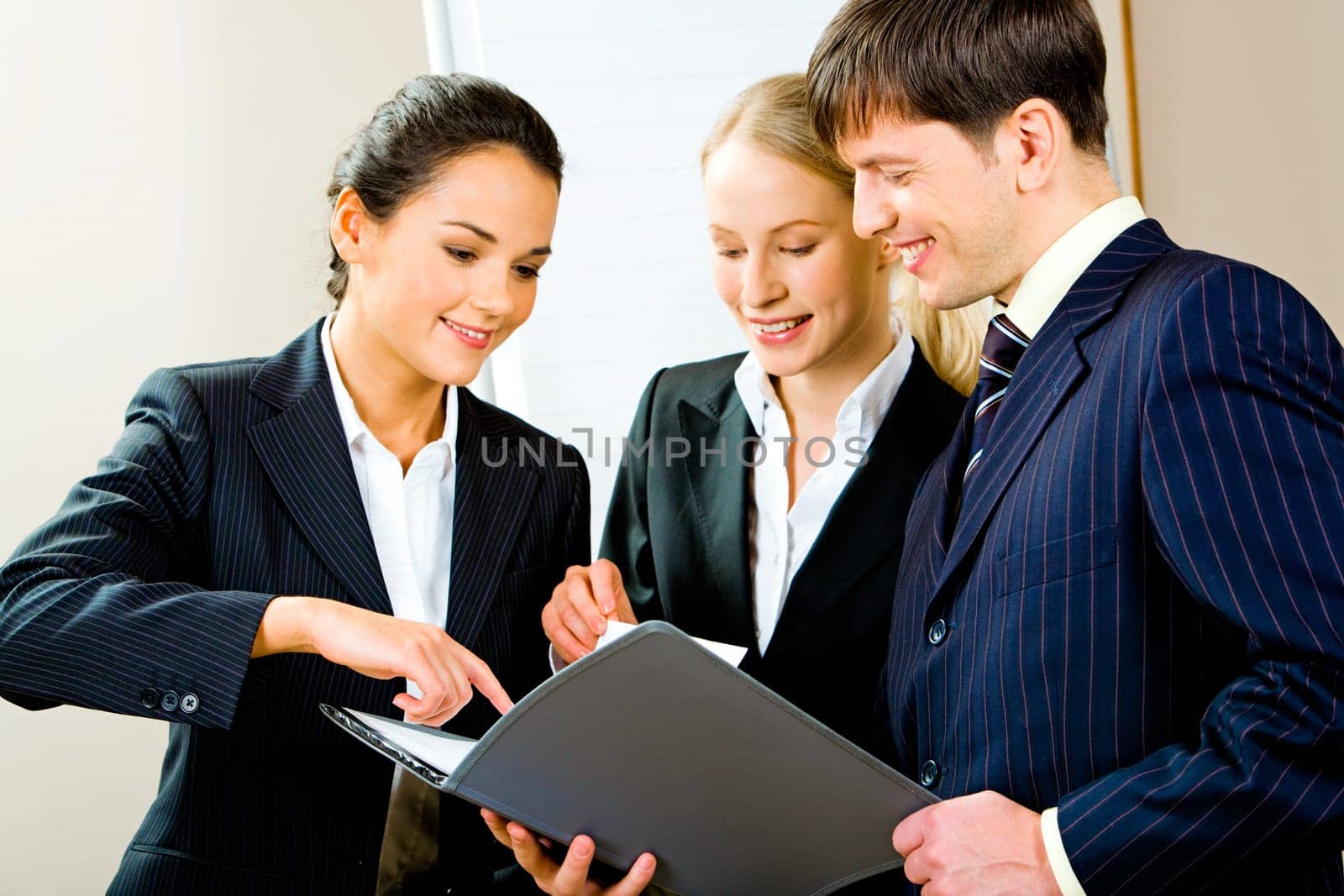 Portrait of three smiling young specialists looking at business plan with one of businesswomen pointing at something in it